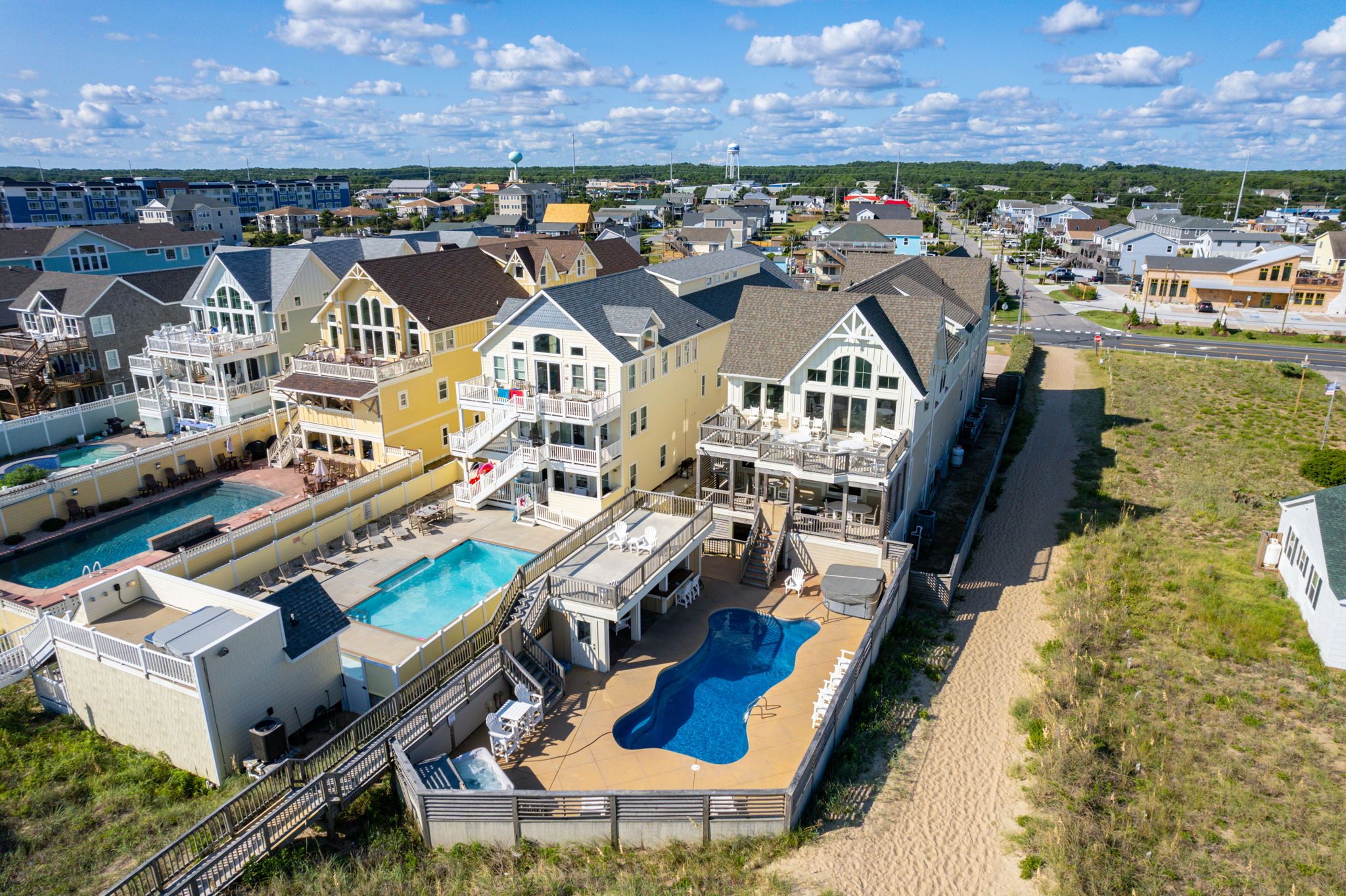 Aerial view of private blue pool at white home next to two other homes with private pools and expansive decks