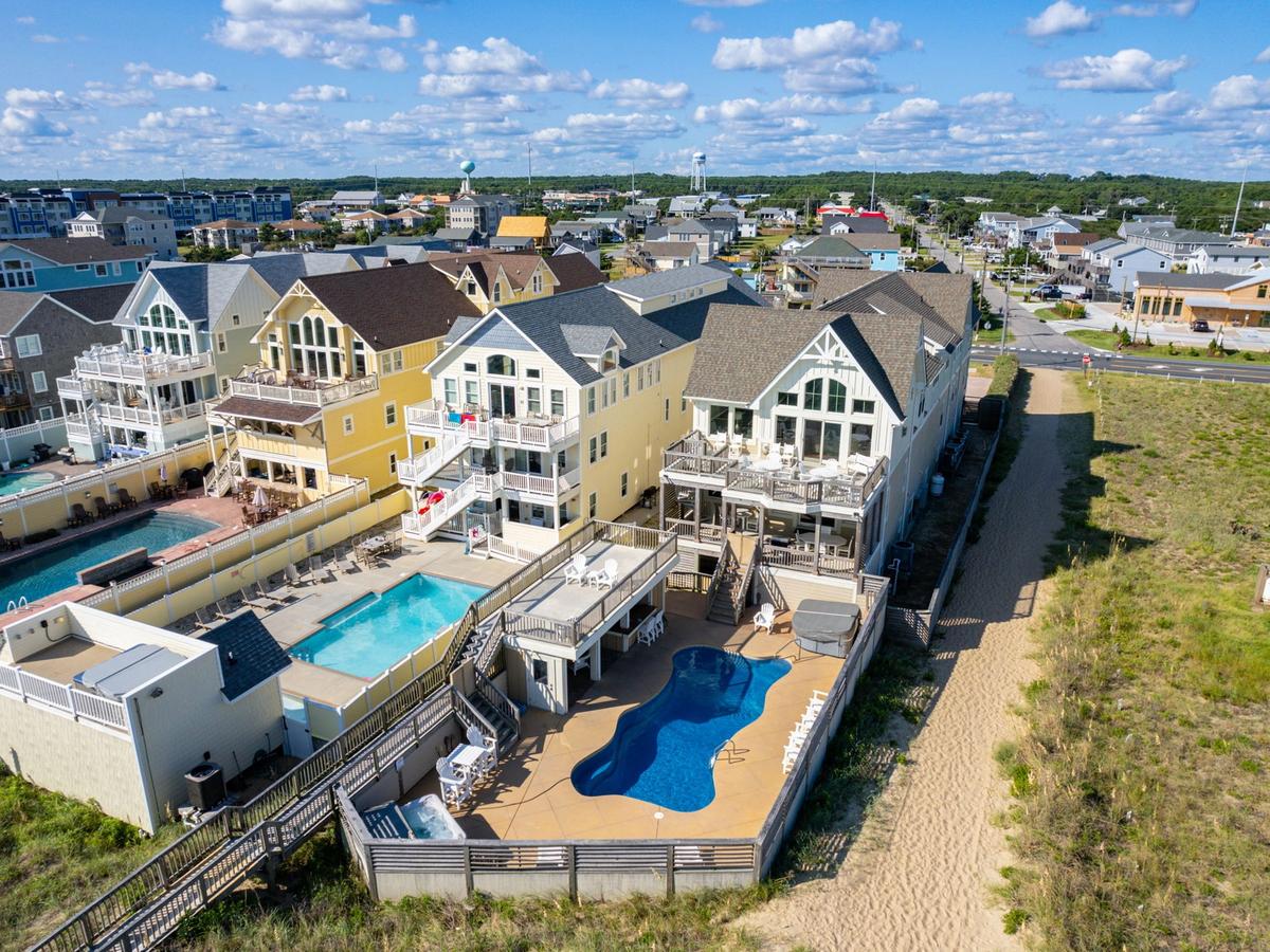 Aerial view of private blue pool at white home next to two other homes with private pools and expansive decks