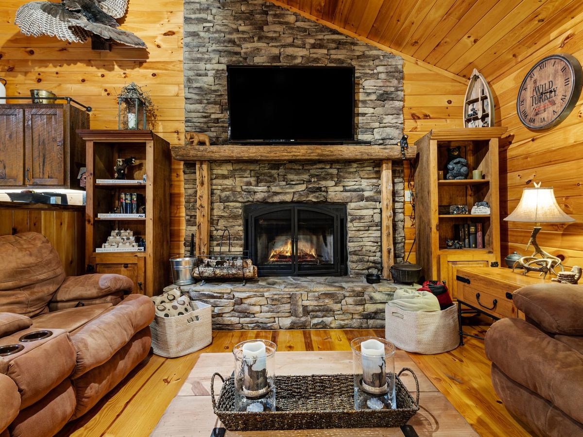 Rustic cabin living room with a stone fireplace, rich wood walls, and cozy recliner ideal for family game nights or a movie after the hot tub. Feels like the mountain home you’ve always wanted.