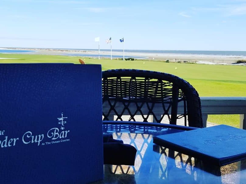 A table set at The Ryder Cup Bar looks out onto the golf green and the ocean, with flags waving in the sea breeze. One of the best views for food and fairways.