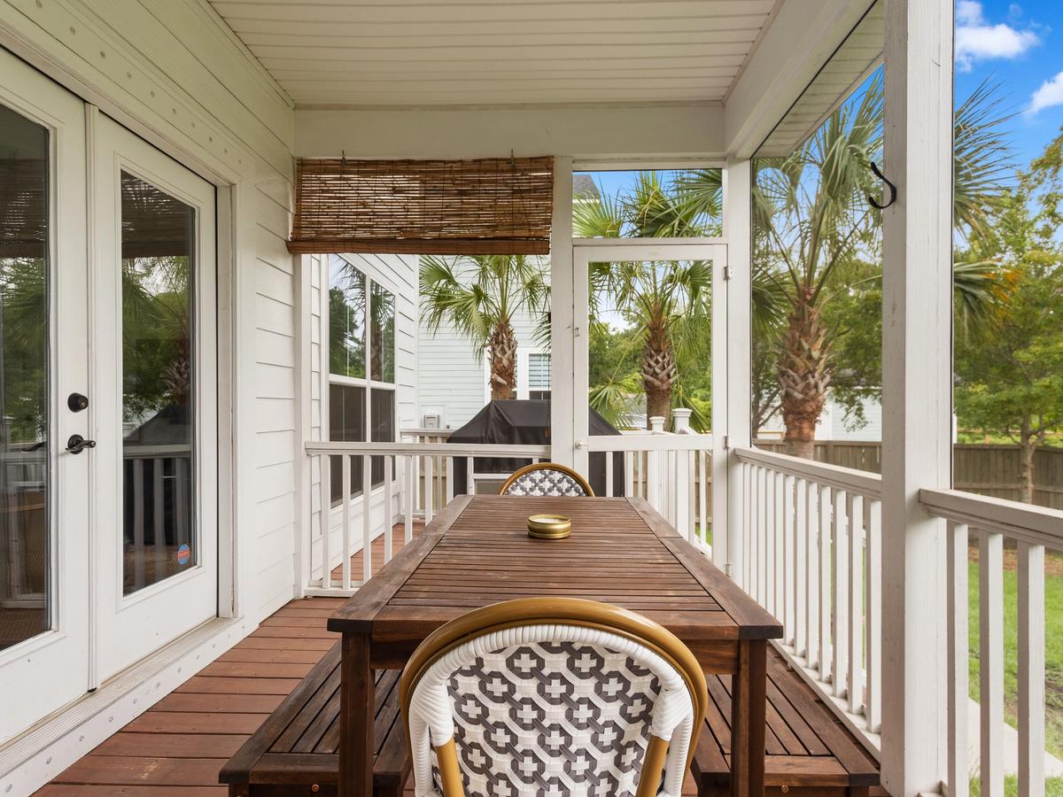 A cozy screened-in porch features a wooden dining table with patterned chairs, surrounded by white railings and palm trees in the backyard.