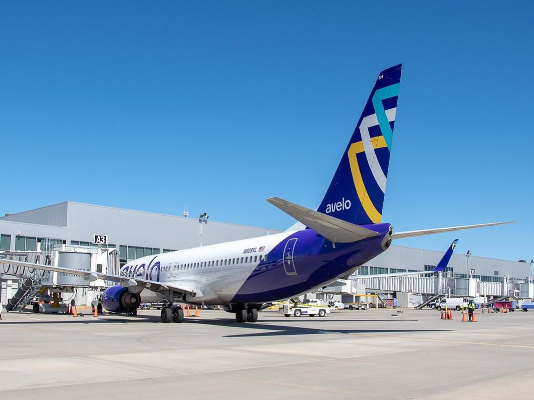 A modern Avelo airplane parked at the gate on a sunny day, ready for passengers to board. Flying into the Bahamas is simple with direct flights from major U.S. cities.