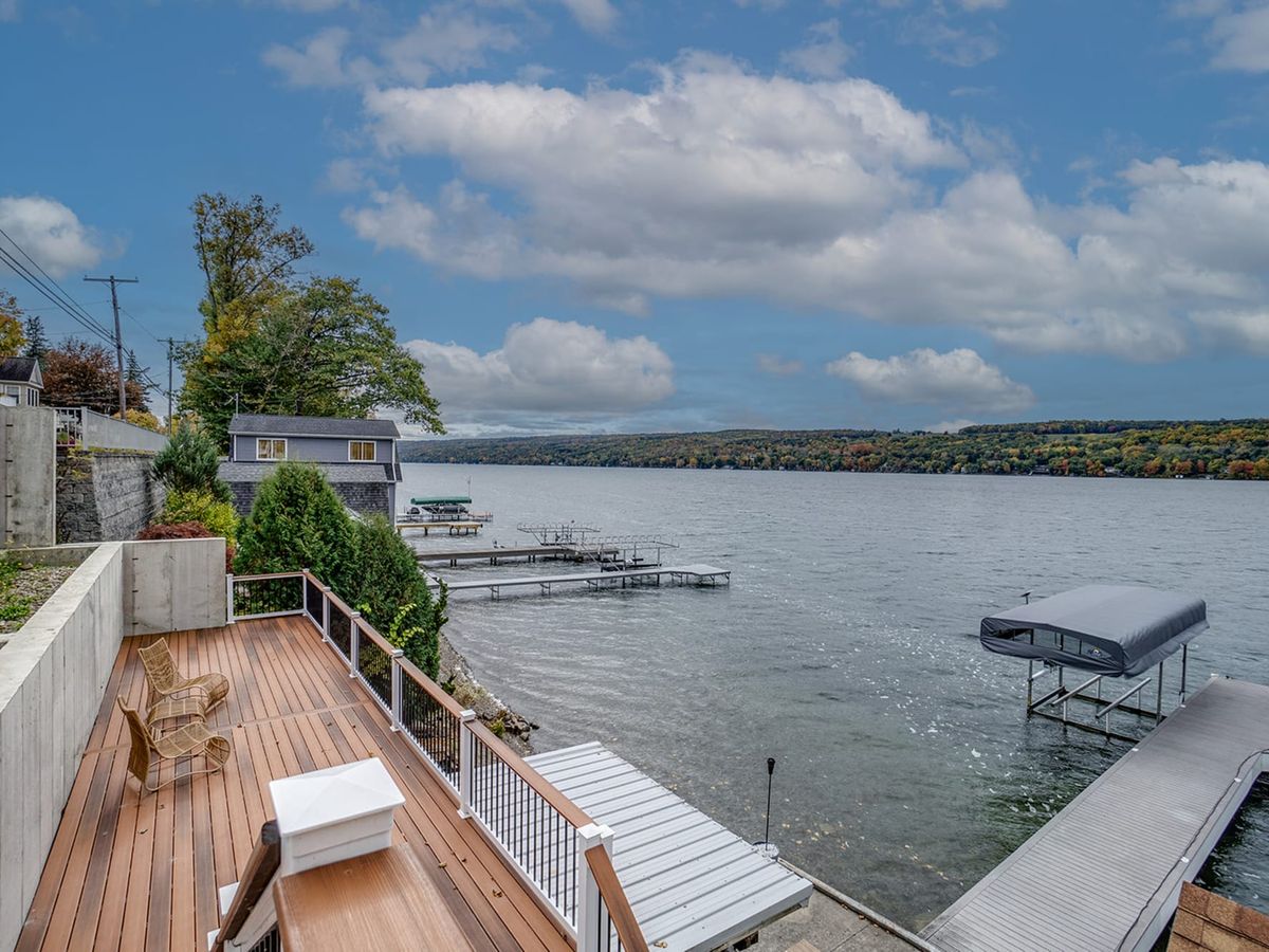 A lakeside deck with chairs overlooks calm waters and nearby docks under a partly cloudy sky. This outdoor space invites guests to unwind with a view, enjoy morning coffee, or watch the sunset over the lake.