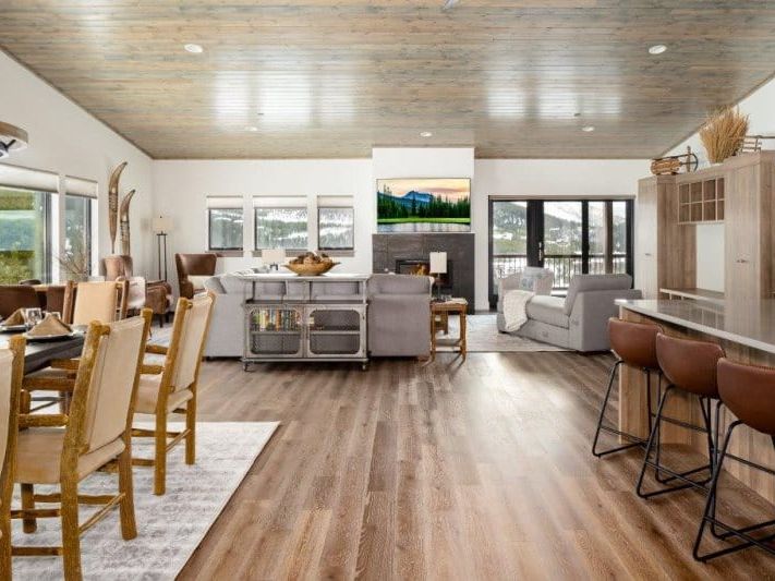 An open-concept mountain home with a modern rustic design features a dining area, cozy living room with fireplace, and kitchen with bar seating, all framed by large windows and scenic views.