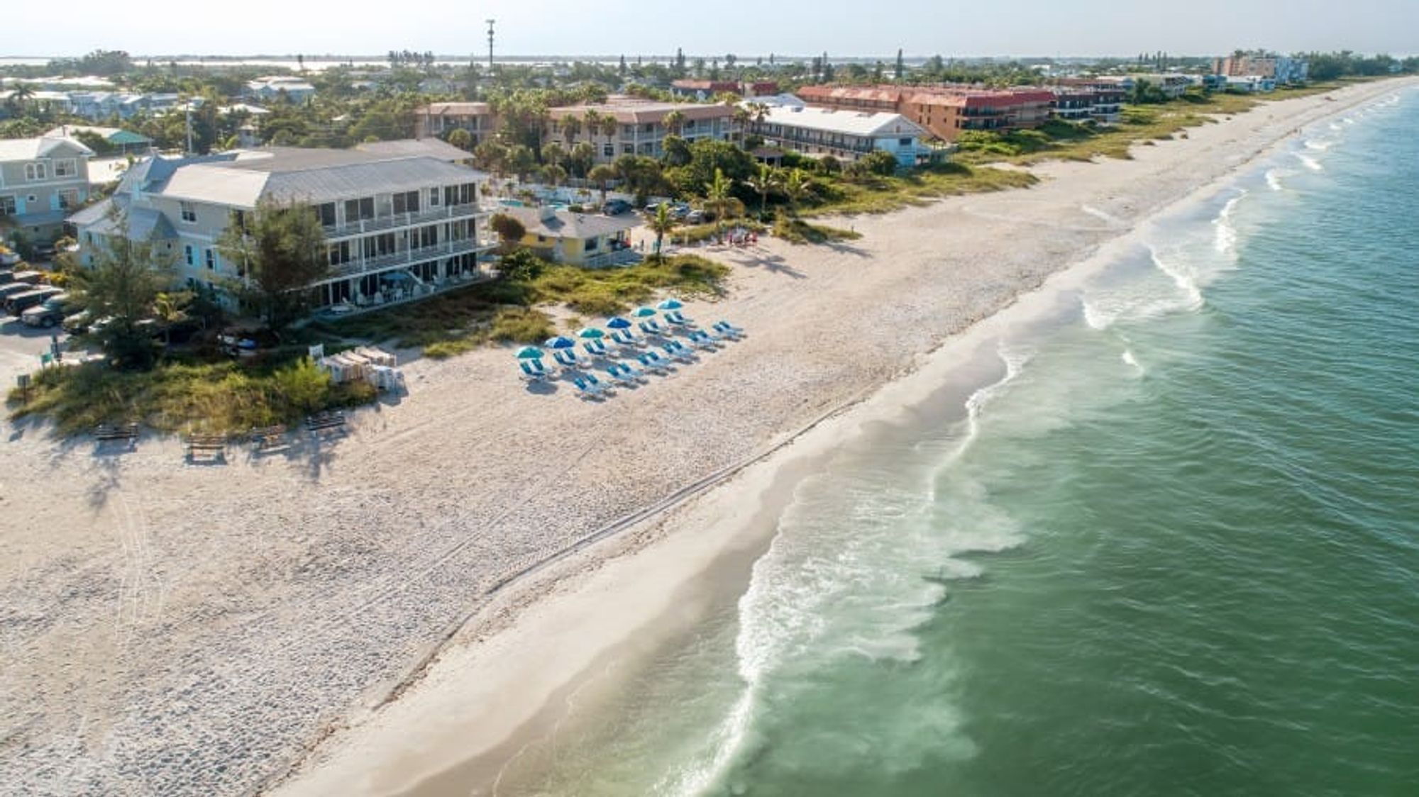 Aerial view of a beachfront resort on Anna Maria Island with turquoise waters, white sand, and rows of beach chairs.