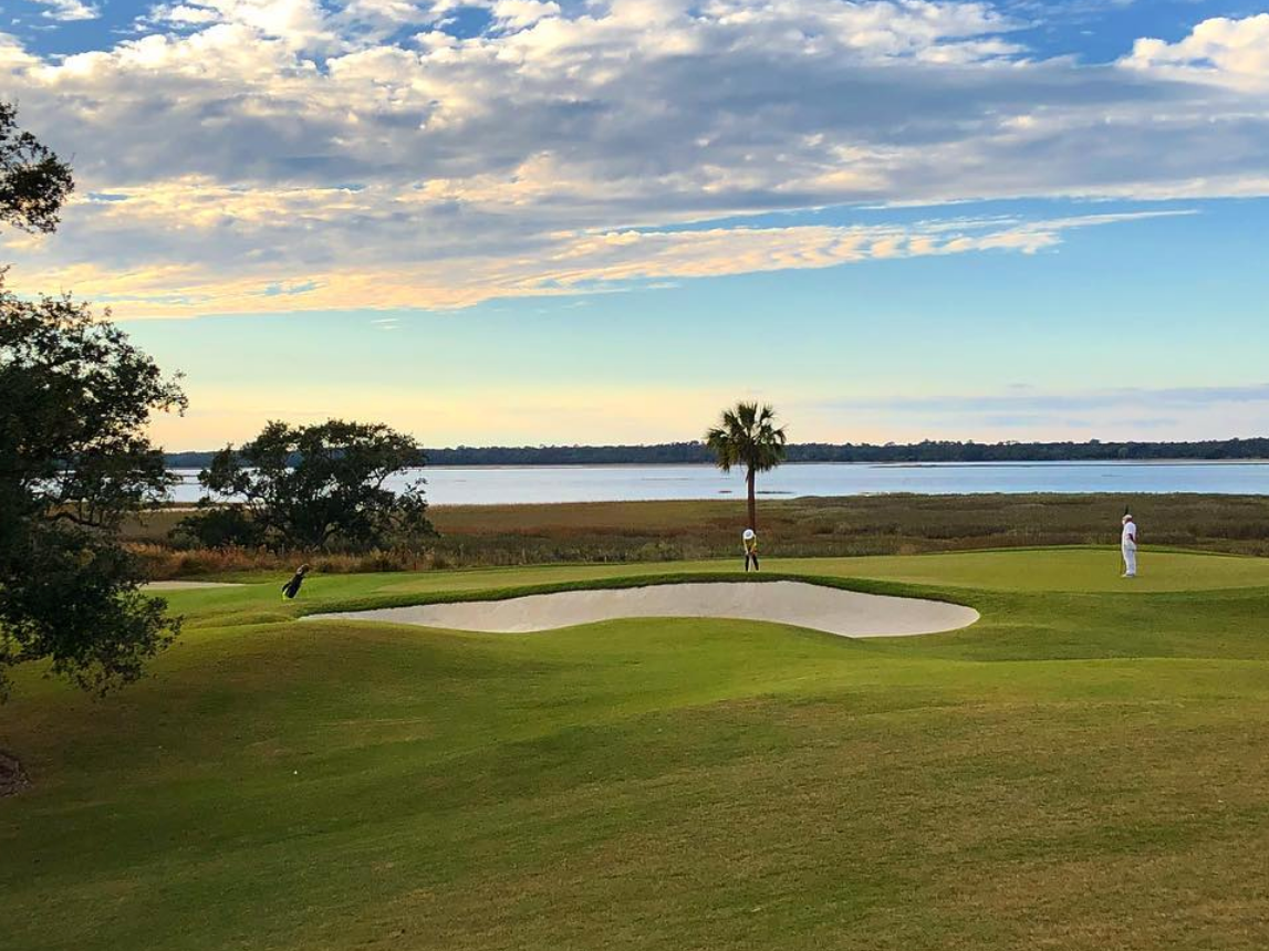 People on golf course hitting golf balls with palm trees and water in background