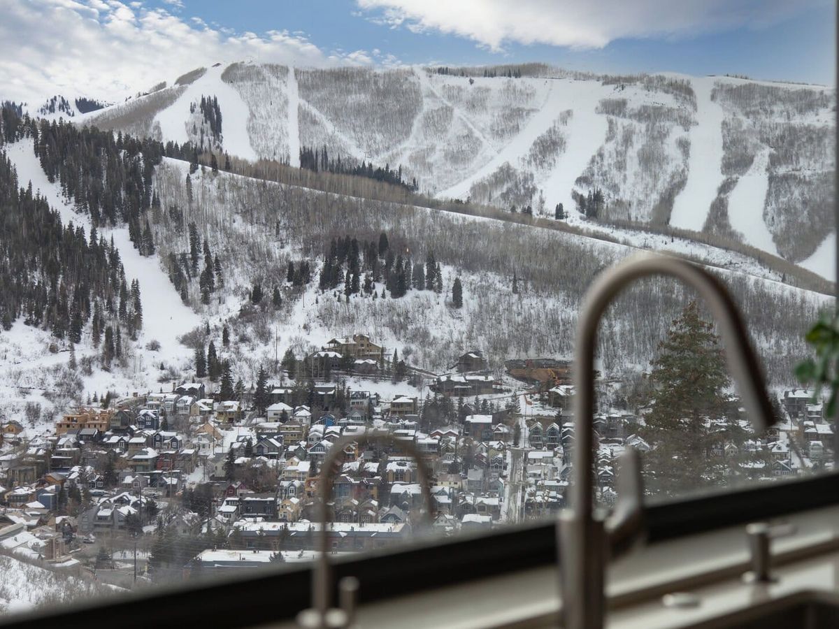 Snowy view from the sink window of snowy mountaintops, building, and trees in Park City