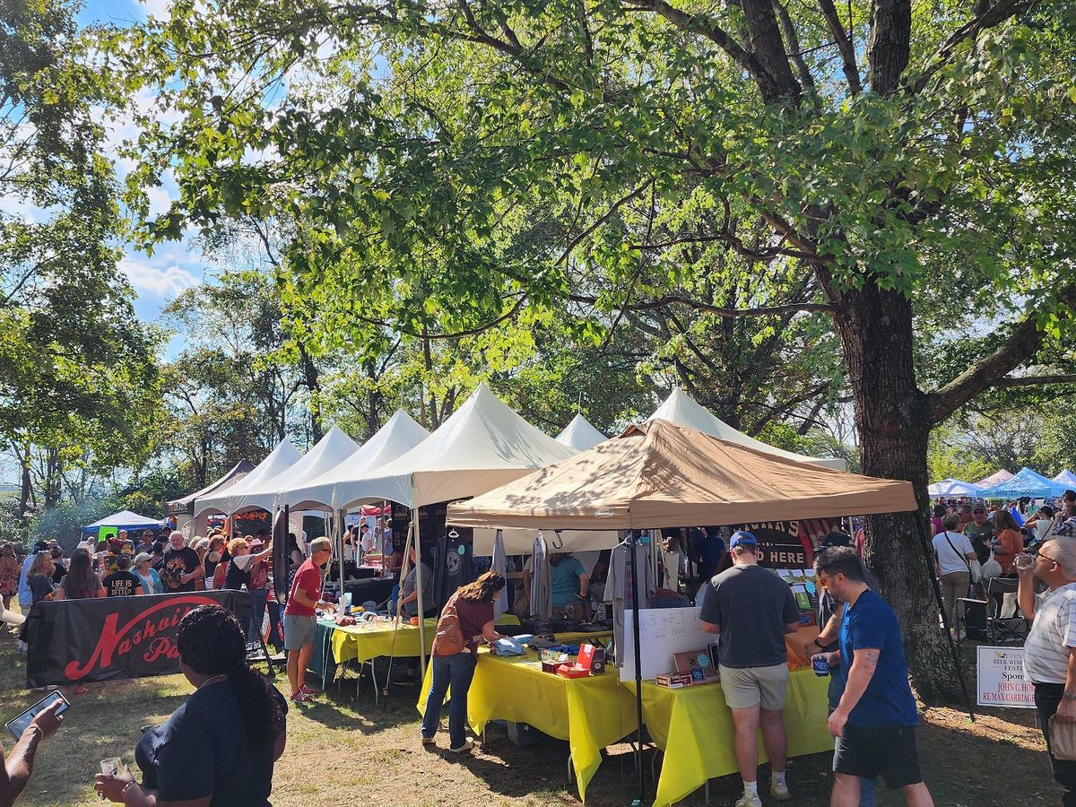 Crowds gather under rows of festival tents, enjoying drinks, food, and sunny weather at the Tennessee Beer, Wine, and Shine Festival. People chat, taste samples, and explore local vendors under the big shade trees. The whole scene has a lively, friendly vibe perfect for a fall day out.
