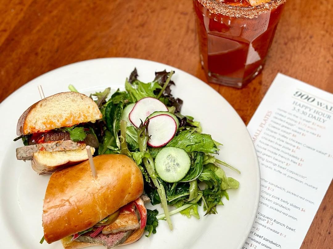 Fresh artisan sandwich with crisp greens and pickled vegetables, served alongside a Bloody Mary topped with grilled shrimp for a savory brunch treat.