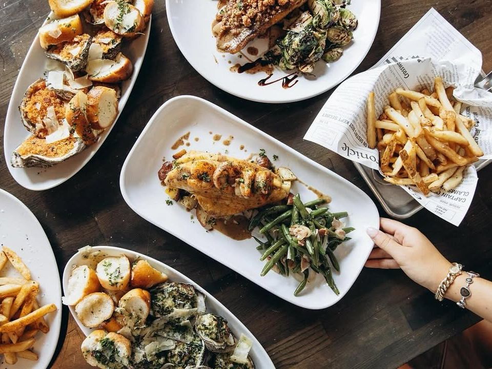 An overhead table view full of Southern-style seafood dishes, chargrilled oysters, fries, and green beans. Perfect for sharing at East Pass Seafood & Oyster House.