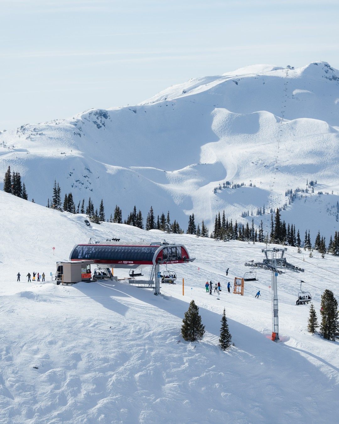 Snow-covered peaks rise above Whistler Blackcomb as skiers line up at the modern chairlift station. Fresh powder blankets the mountain, creating the perfect setting for winter adventures in Whistler, BC. This iconic ski resort is known for world-class runs and stunning alpine views.