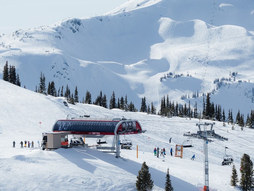Snow-covered peaks rise above Whistler Blackcomb as skiers line up at the modern chairlift station. Fresh powder blankets the mountain, creating the perfect setting for winter adventures in Whistler, BC. This iconic ski resort is known for world-class runs and stunning alpine views.