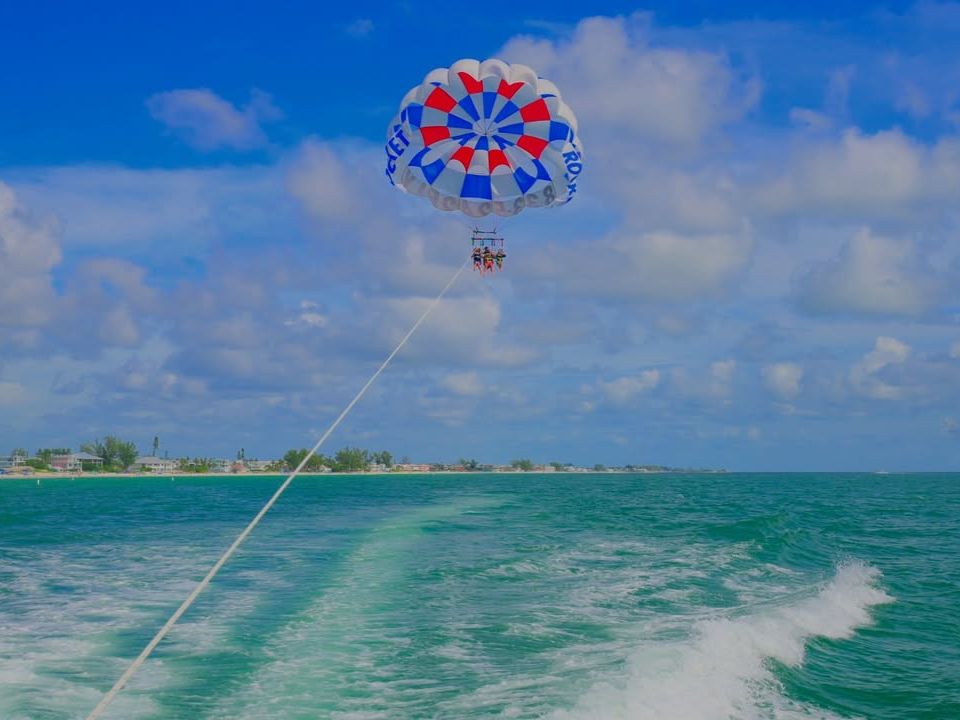 Two people parasail above the Gulf with Sea Rocket Adventures, offering stunning bird’s-eye views of Anna Maria Island.
