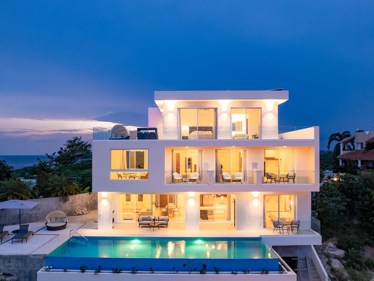 This modern beachfront villa lights up beautifully at dusk with a glowing pool, sleek lounge chairs, and tropical palms swaying in the breeze. A dreamy spot for group getaways and relaxing under the stars.