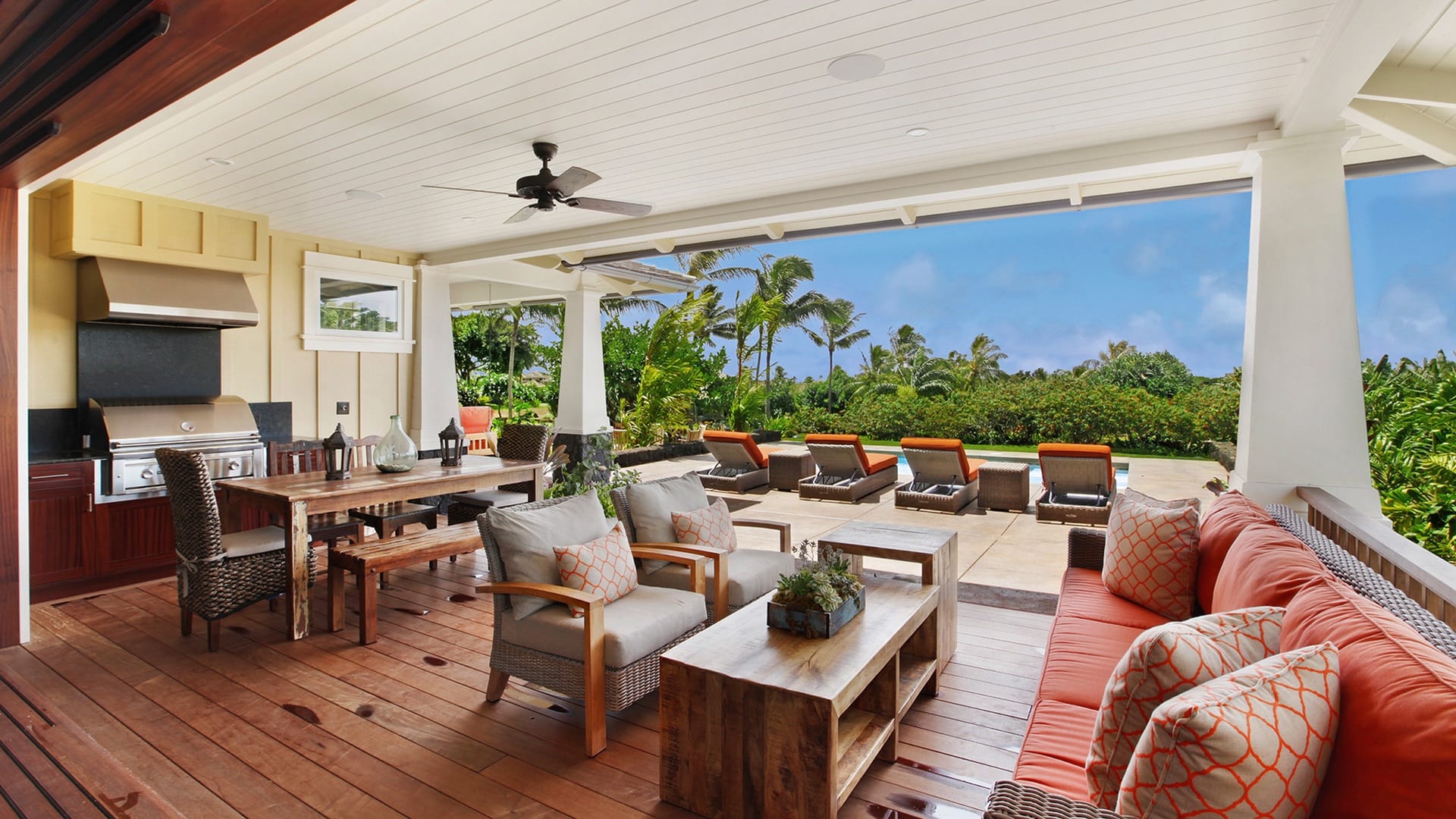 Large, outdoor living room view of open-air patio that overlooks lounge chairs by pool and palm trees