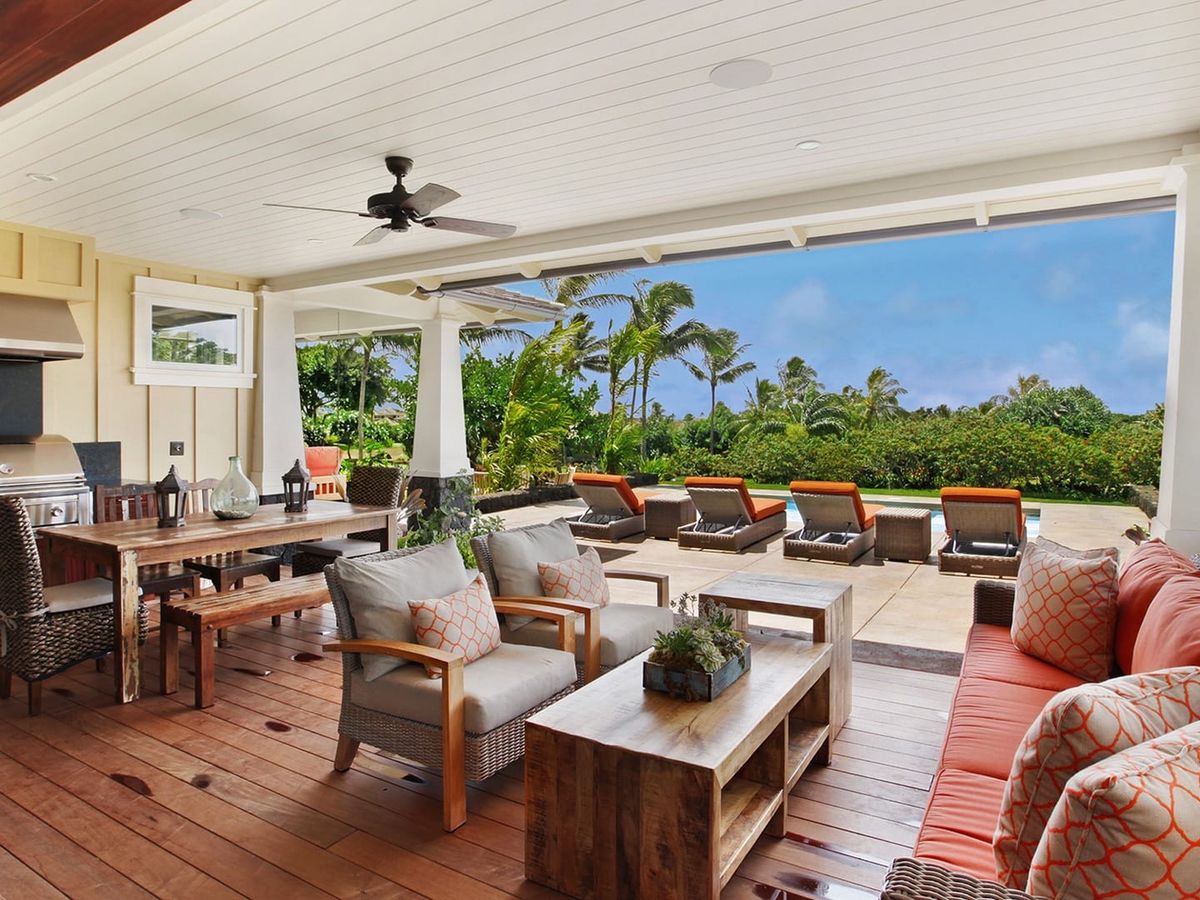 Large, outdoor living room view of open-air patio that overlooks lounge chairs by pool and palm trees