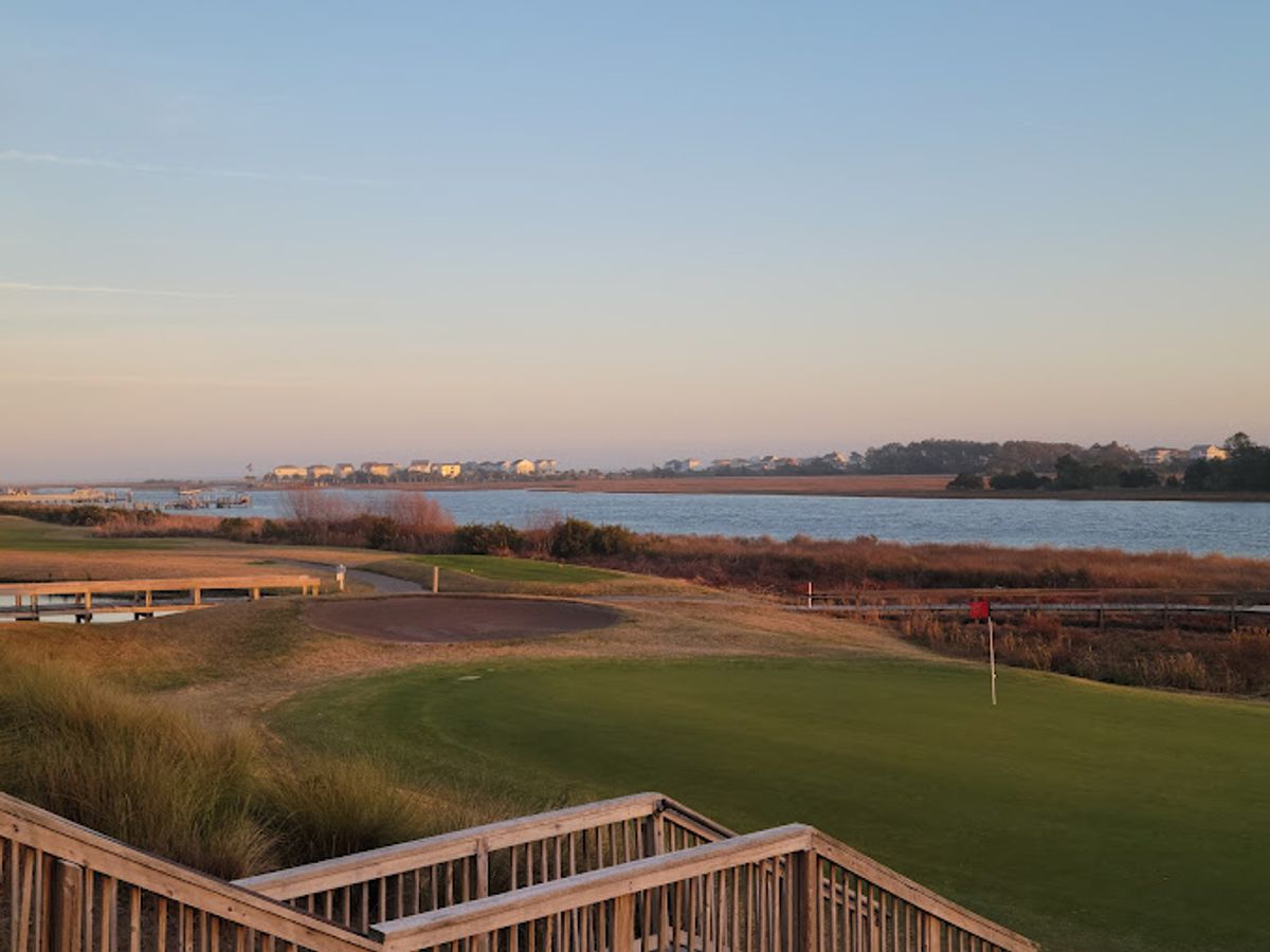 A scenic golf green at The Links at Brick Landing overlooks a calm river and wide marsh views. The peaceful coastal setting makes it a relaxing spot for a round of golf.