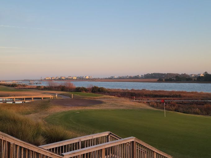A scenic golf green at The Links at Brick Landing overlooks a calm river and wide marsh views. The peaceful coastal setting makes it a relaxing spot for a round of golf.