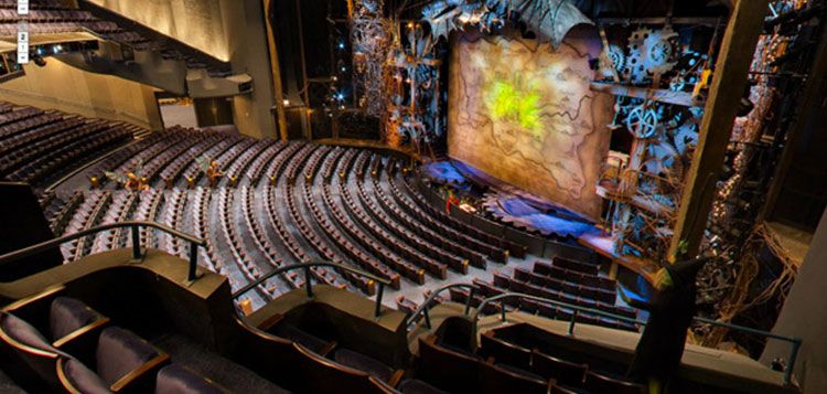 A sweeping view of the Gershwin Theatre shows its grand seating area curving toward a brightly lit stage set for the musical Wicked. The ornate backdrop, filled with gears and glowing green light, adds a magical feel even before the show begins. The spacious auditorium makes it clear why this Broadway venue is so iconic.