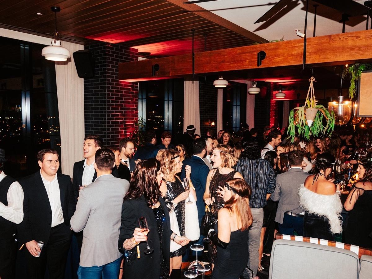 A lively rooftop party at Virgin Hotels Nashville with guests dressed up, chatting, and enjoying drinks under warm city lights. This stylish venue is popular for nightlife, social events, and skyline views in downtown Nashville.