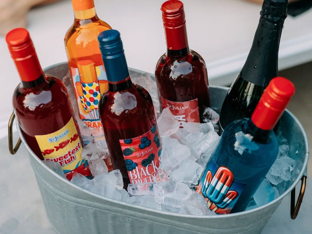 A bucket filled with colorful bottles of St. Julian wines rests on ice, perfect for a summer gathering. Southwest Michigan wineries invite you to sip, taste, and discover your new favorite blend.