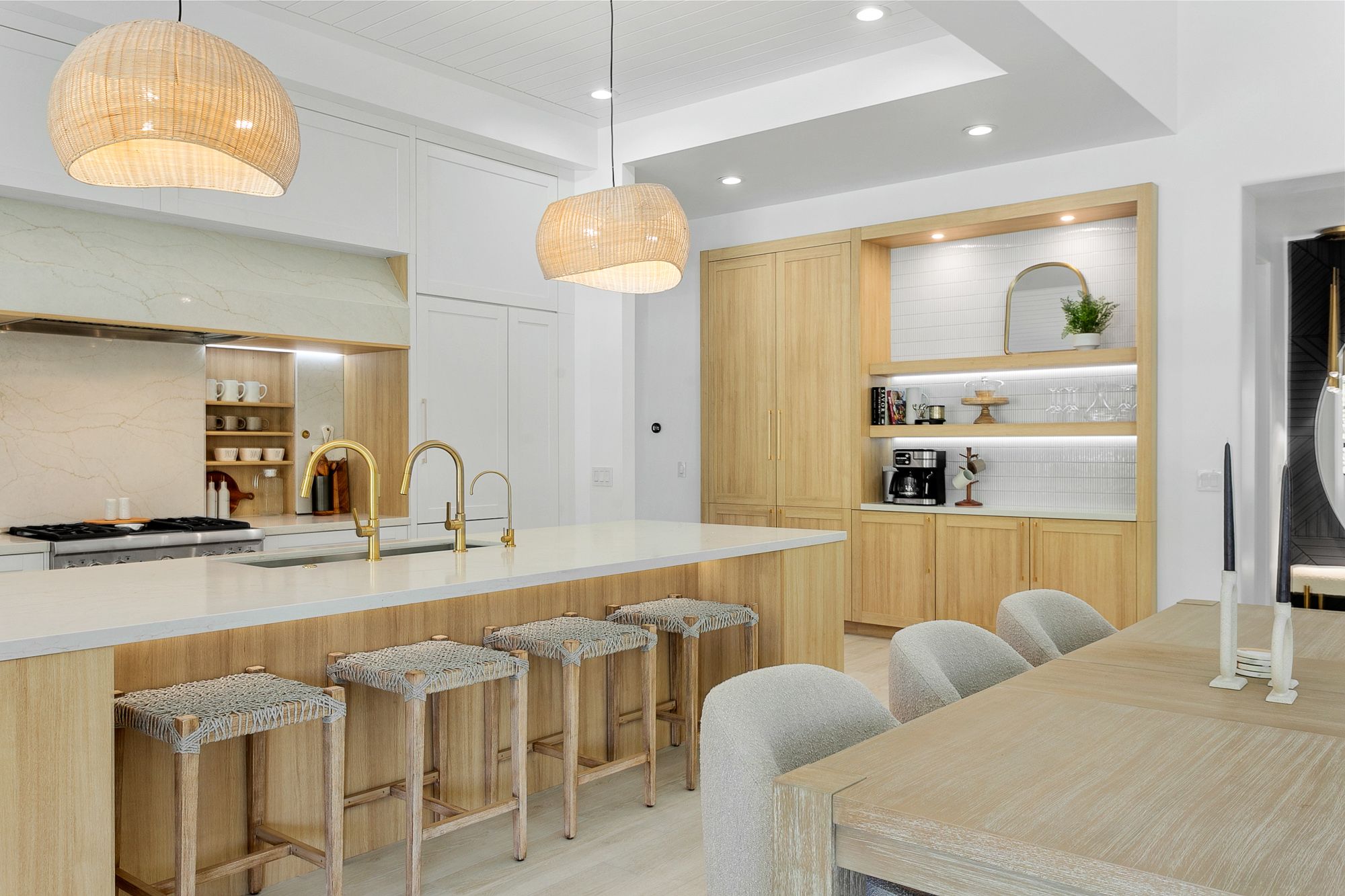 A bright, modern kitchen featuring warm wood cabinetry, a spacious island with brass fixtures, woven barstools, and soft pendant lighting for an inviting, elevated design.