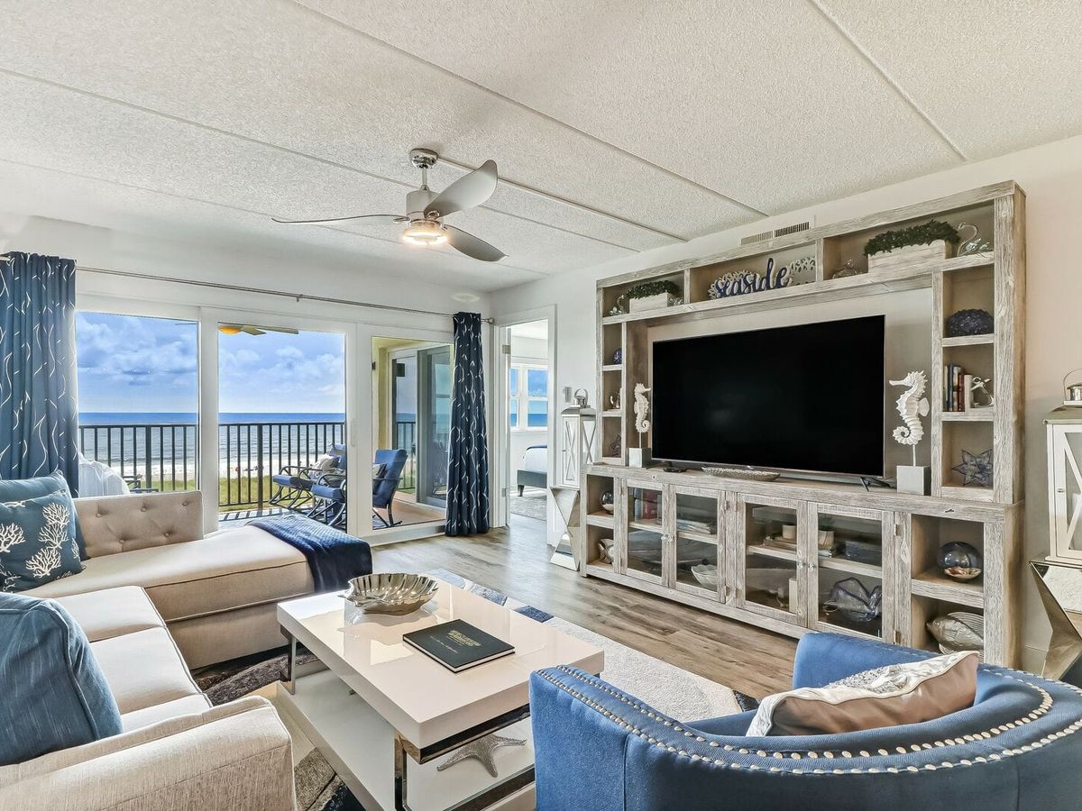 Cozy oceanfront living room with plush seating, a giant TV, and nautical décor. Wide glass doors lead to a private balcony, making it easy to soak in the beach vibes all day.