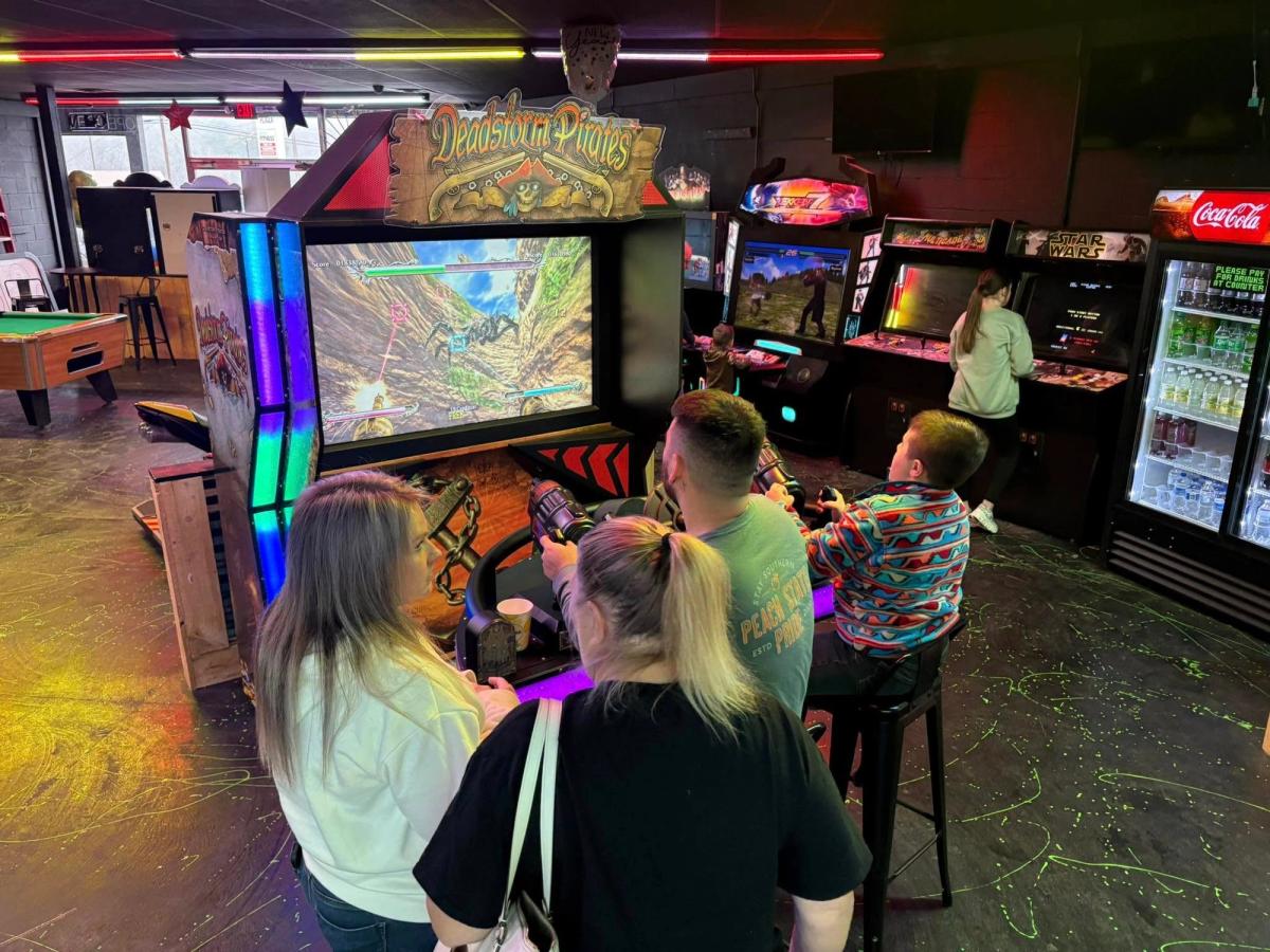 Families enjoy classic arcade games inside a lively entertainment center. Bright lights and colorful machines fill the room, offering fun for all ages. Kids and adults alike gather around games, creating a cheerful atmosphere.