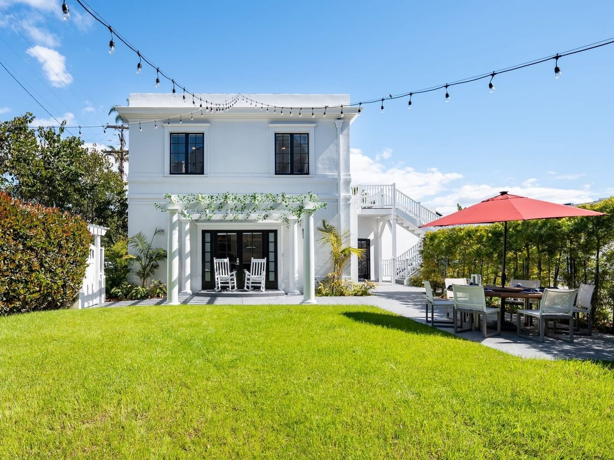 This bright white villa has string lights, a red umbrella patio, and a large green lawn made for gatherings. With its cozy charm and space to entertain, it’s perfect for family reunions or special getaways.