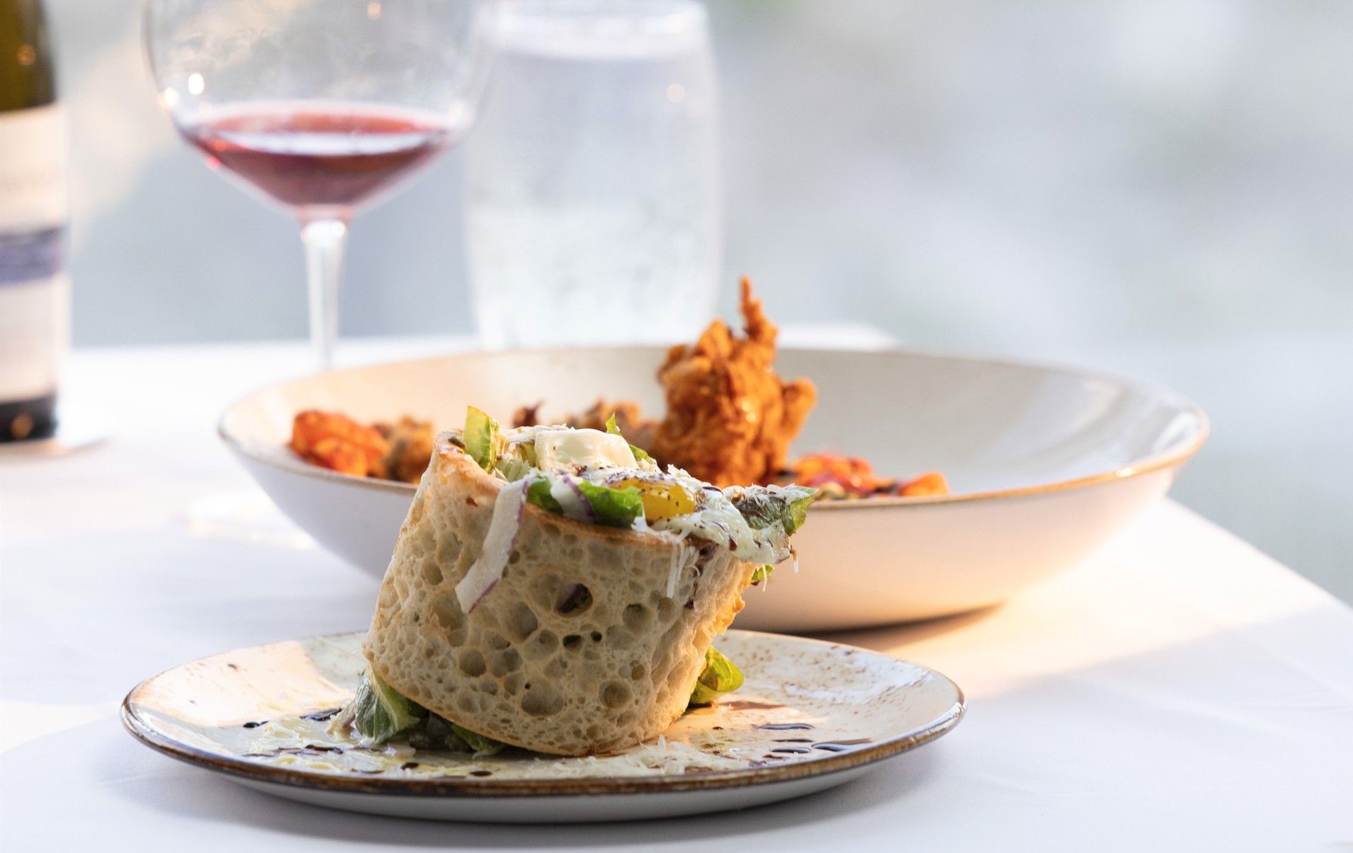 Outdoor waterfront dining with a relaxed coastal vibe, featuring wine glasses and shared appetizers on a sunny patio. This spot is perfect for enjoying fresh flavors while overlooking the water during a laid-back lunch or sunset drink. It captures the easy, social dining experience many visitors look for on a coastal getaway.