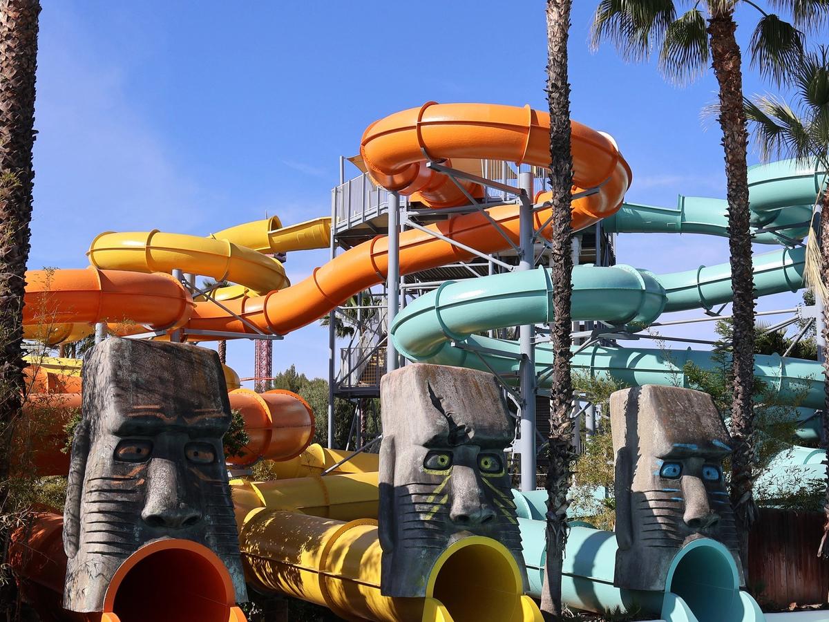 Bright orange, yellow, and teal waterslides twist and turn at a Southern California theme park. Palm trees and carved tiki faces add a tropical feel to this fun water attraction