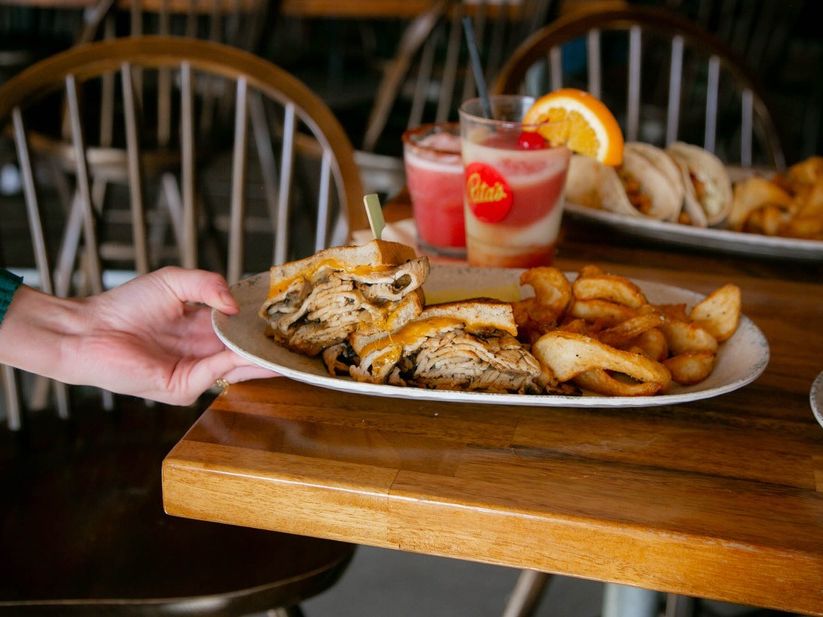 A delicious grilled chicken sandwich with melted cheese and crispy curly fries is served fresh alongside colorful frozen cocktails at Rita’s Seaside Grille, perfect for a laid-back beach meal.
