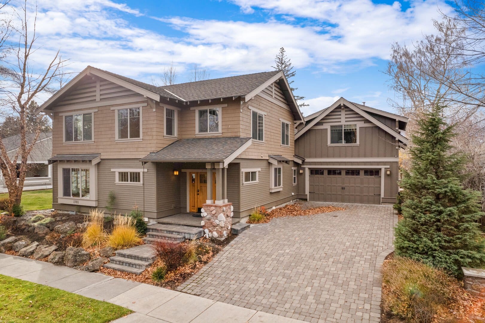 A beautifully crafted mountain home with a spacious driveway and landscaped front yard framed by evergreens. Its earthy tones and large windows give it a cozy yet modern feel ideal for family stays.