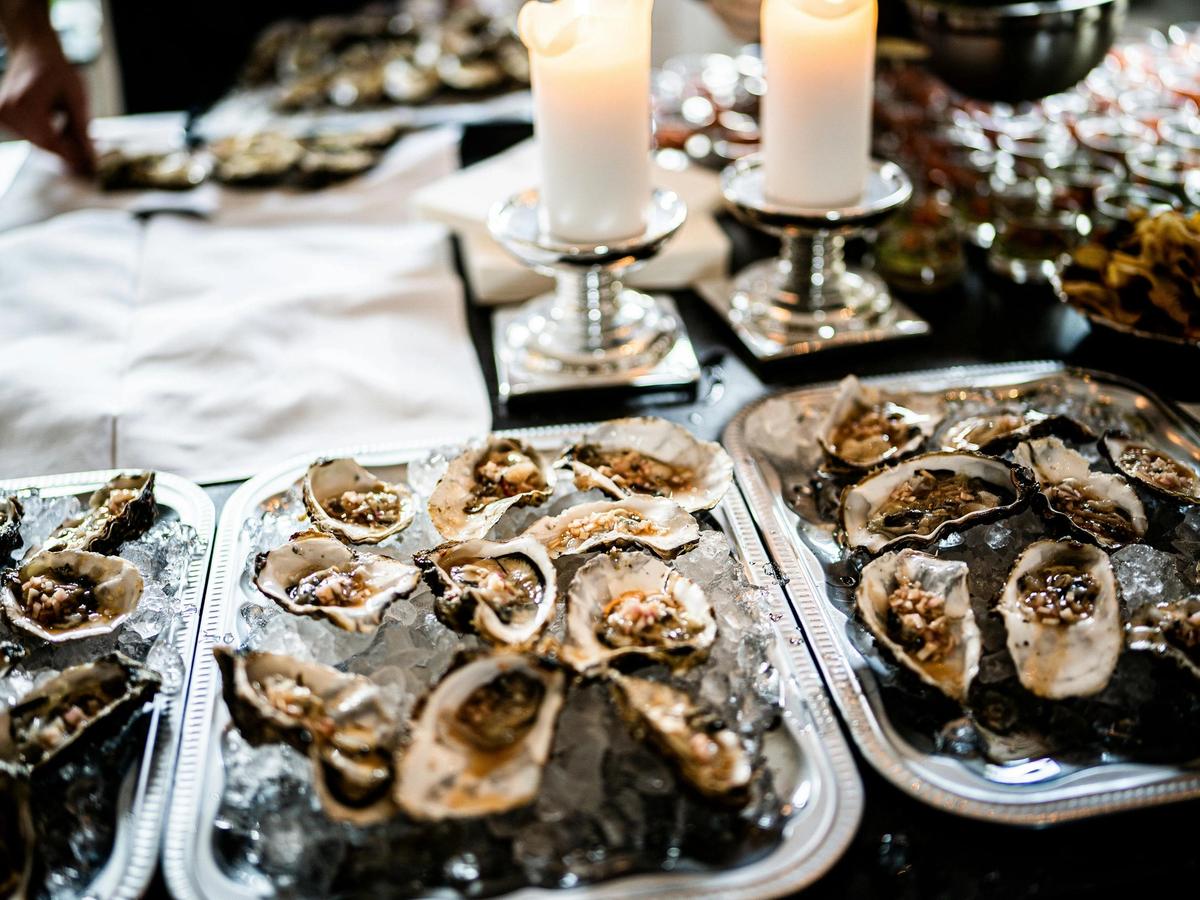 Fresh oysters served on ice with savory toppings, elegantly presented on silver trays beside glowing candles for a refined coastal dining experience.