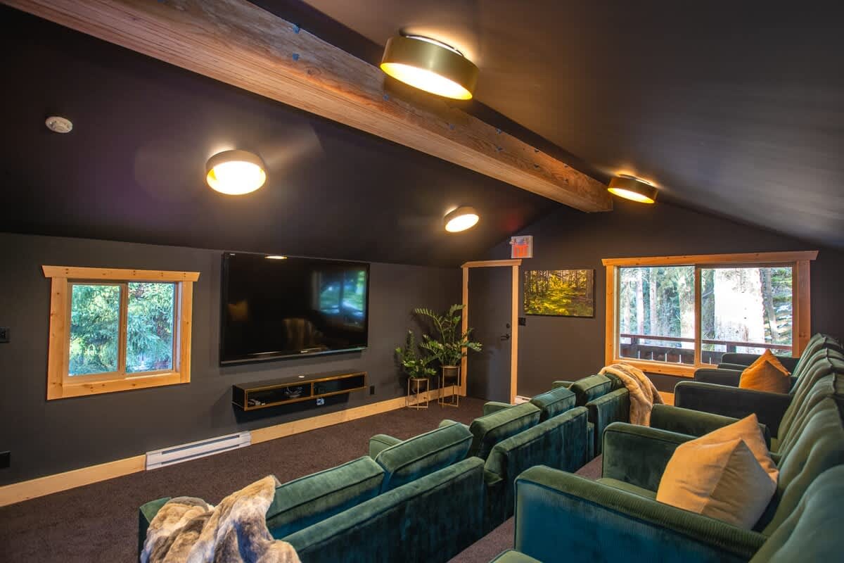 Cozy private home theater with tiered green velvet seating, dark walls, warm lighting, and a large wall-mounted screen.