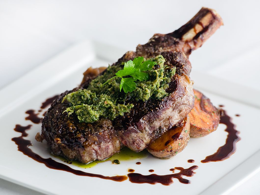 A juicy bone-in ribeye steak served with chimichurri and sweet potatoes, plated with rich balsamic glaze. A fine dining favorite at Bijoux in Destin.