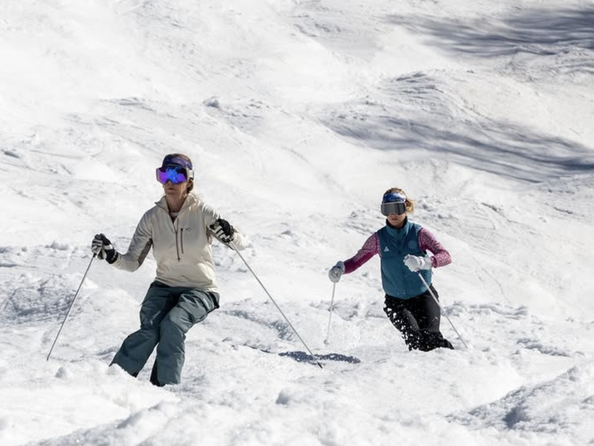 Two skiers in colorful winter gear navigate a snowy slope together on a bright, sunny day.