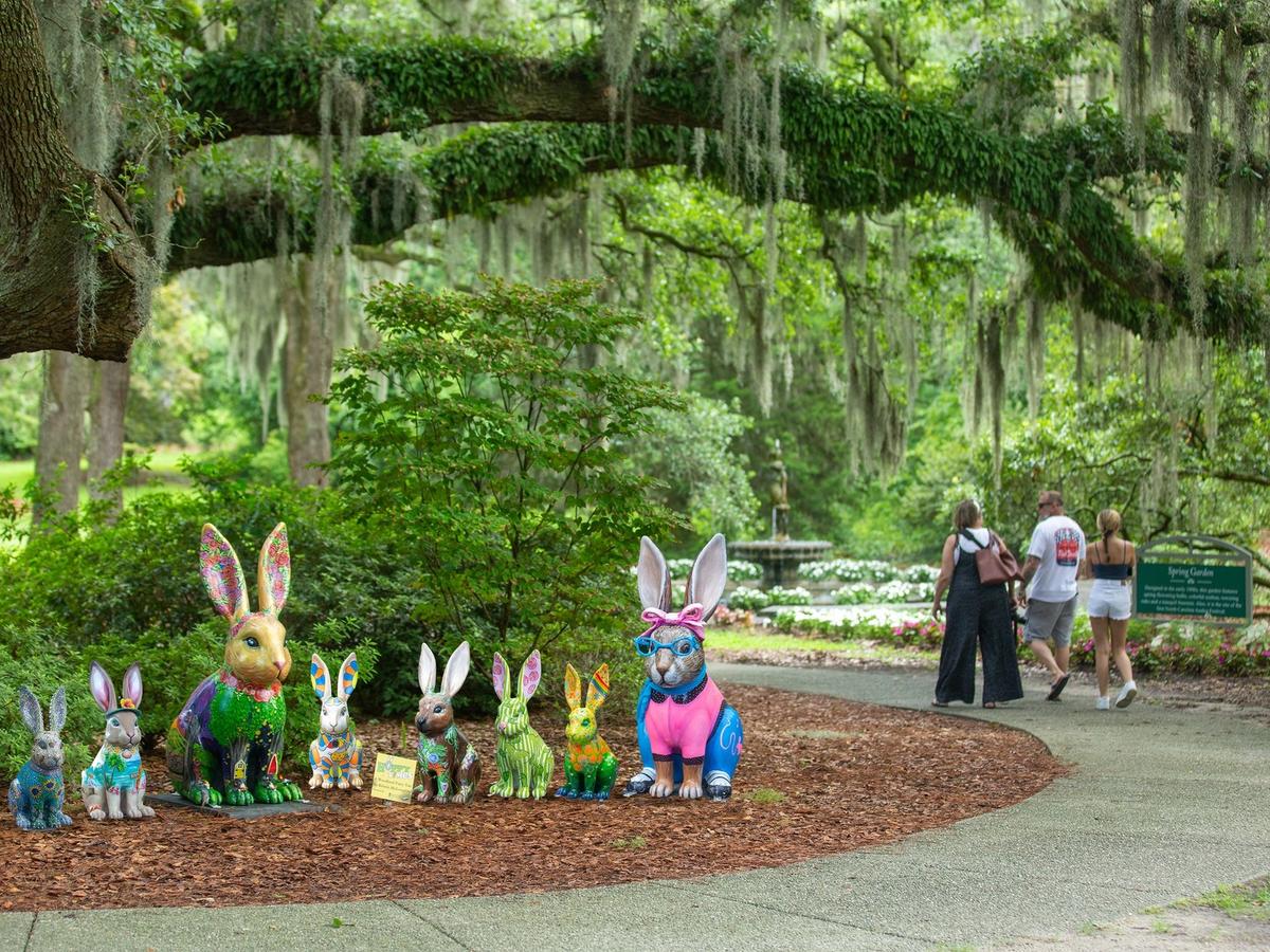 Colorful rabbit statues line a peaceful walking path at Airlie Gardens, surrounded by lush greenery and hanging Spanish moss. Visitors stroll through the garden, enjoying the quiet nature views and unique outdoor art displays.