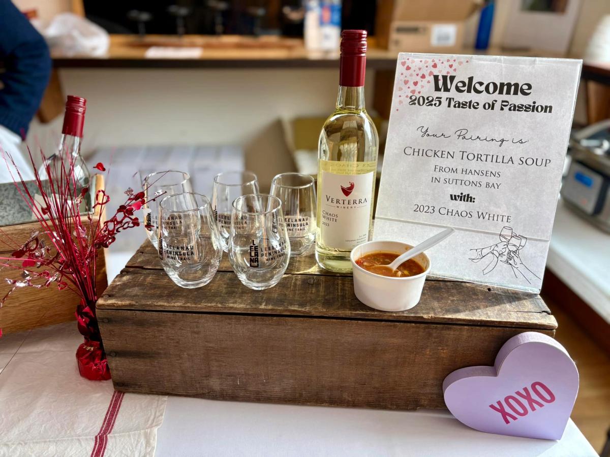 A wine tasting setup features Verterra’s Chaos White wine paired with a warm bowl of chicken tortilla soup. Glasses with the Leelanau Peninsula logo and festive Valentine’s Day decorations complete the display. This cozy presentation reflects Michigan’s Traverse Wine Coast hospitality.