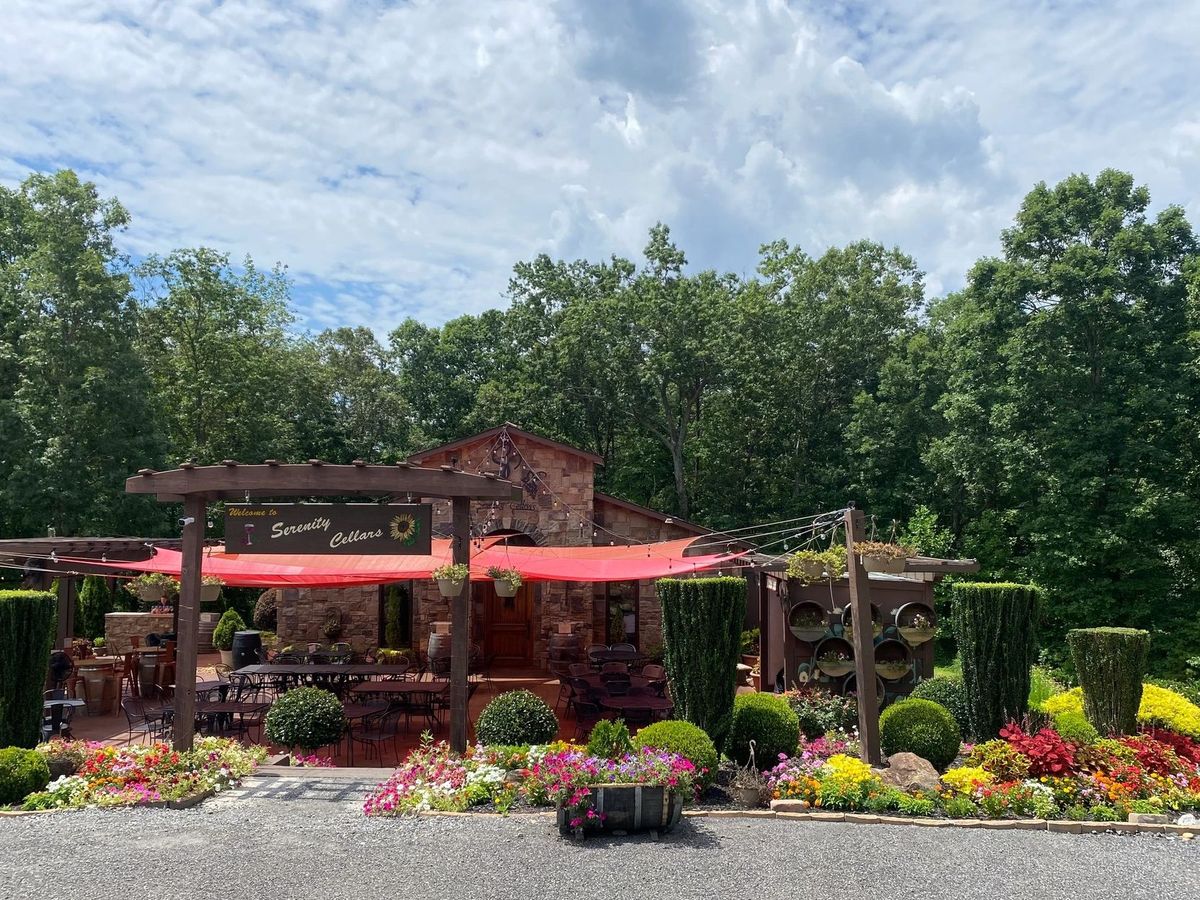 Serenity Cellars features a charming outdoor space filled with colorful flowers, shaded seating, and stone details. The red canopy gives the area a warm, lively feel. It looks like a peaceful place to sit back and enjoy a glass of wine.