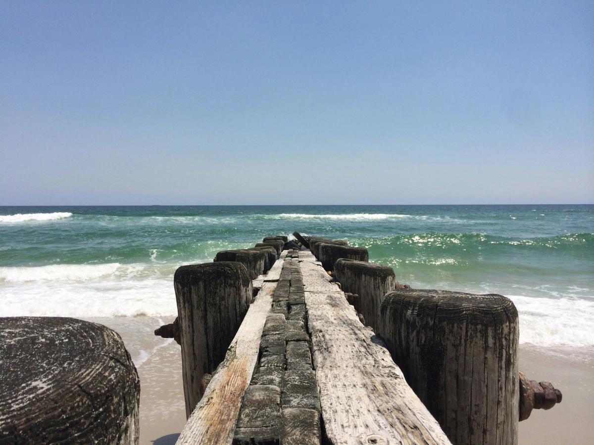 Weathered wooden pier extending into turquoise ocean waves under a clear blue sky on a sunny day.