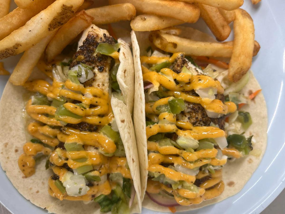 Two grilled fish tacos with spicy orange drizzle and a side of golden fries. A casual and tasty meal from a lively Ocean City sports bar.