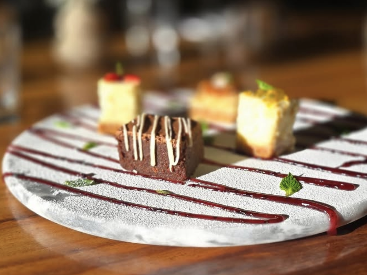 Elegant dessert platter featuring assorted bite-sized cakes and brownies, artfully drizzled with red sauce and garnished with fresh mint on a white plate