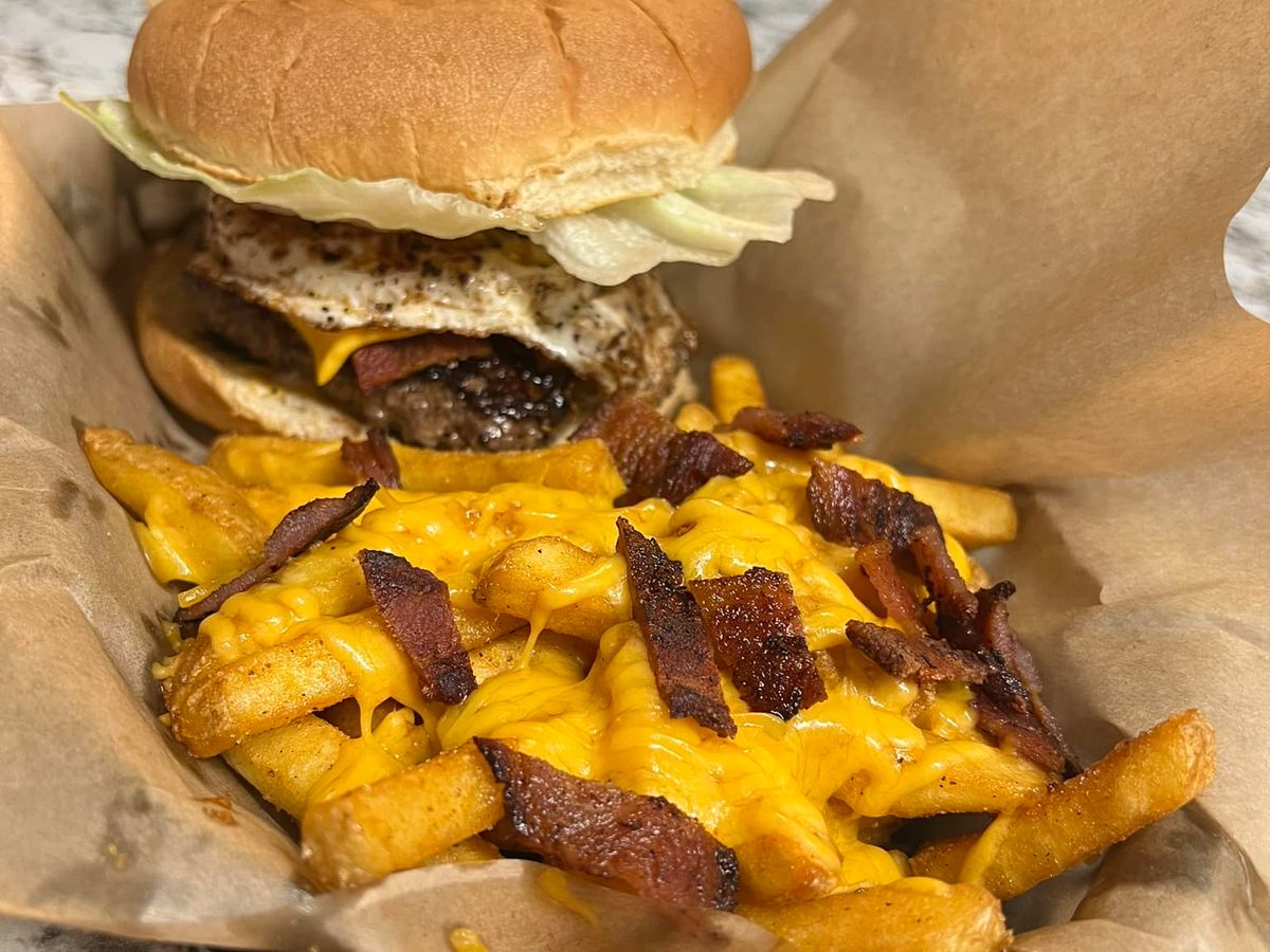 Juicy burger topped with a fried egg and cheddar, paired with cheesy bacon-loaded fries. A rich and indulgent meal perfect for serious burger lovers.