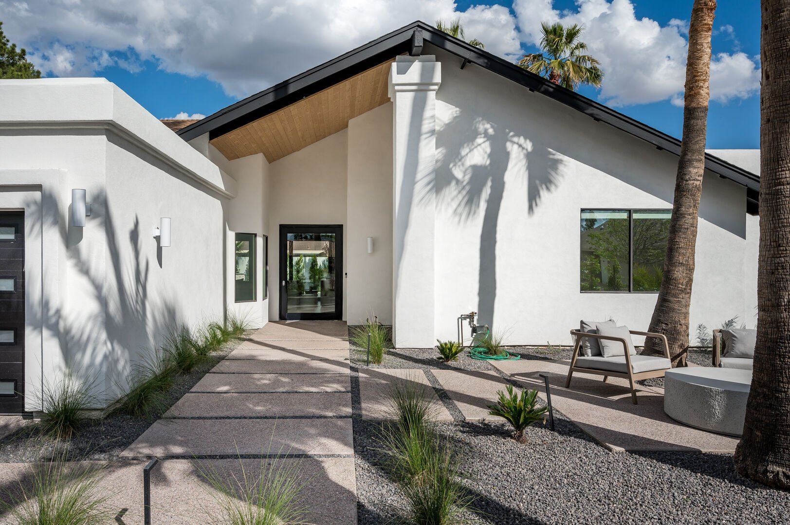 Entryway to white home with door that looks into the home and plants surrounding the walkway