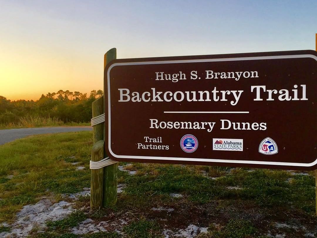 Trailhead sign for Hugh S. Branyon Backcountry Trail at Rosemary Dunes, just before sunset. A great stop for nature lovers exploring Gulf State Park on a budget.