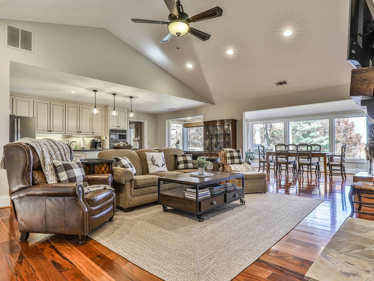 Enchanted Mountain Hideaway in Big Canoe offers a cozy living space with timber beams, a stone fireplace, and plush couches. This rustic gem includes a private hot tub and sweeping views.