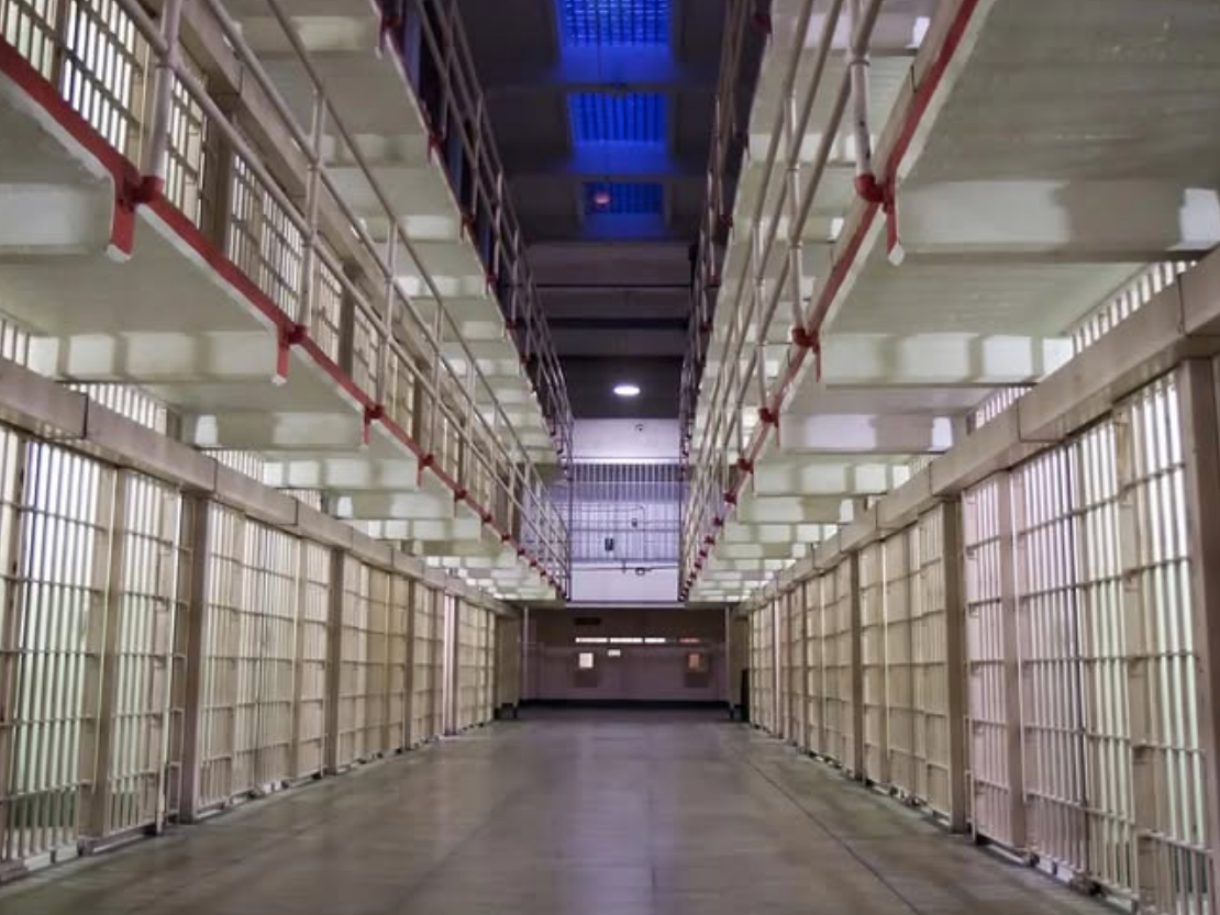 A long corridor of barred prison cells at Alcatraz East Crime Museum, with two tiers of walkways and overhead lighting casting a stark glow.