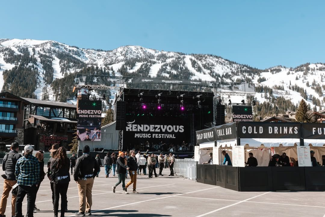 Festivalgoers walk toward the main stage at Rendezvous Music Festival, set against snowy mountain peaks. This outdoor Jackson Hole music festival combines live performances, alpine scenery, and a relaxed winter festival vibe.