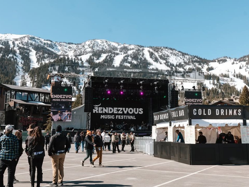 Festivalgoers walk toward the main stage at Rendezvous Music Festival, set against snowy mountain peaks. This outdoor Jackson Hole music festival combines live performances, alpine scenery, and a relaxed winter festival vibe.